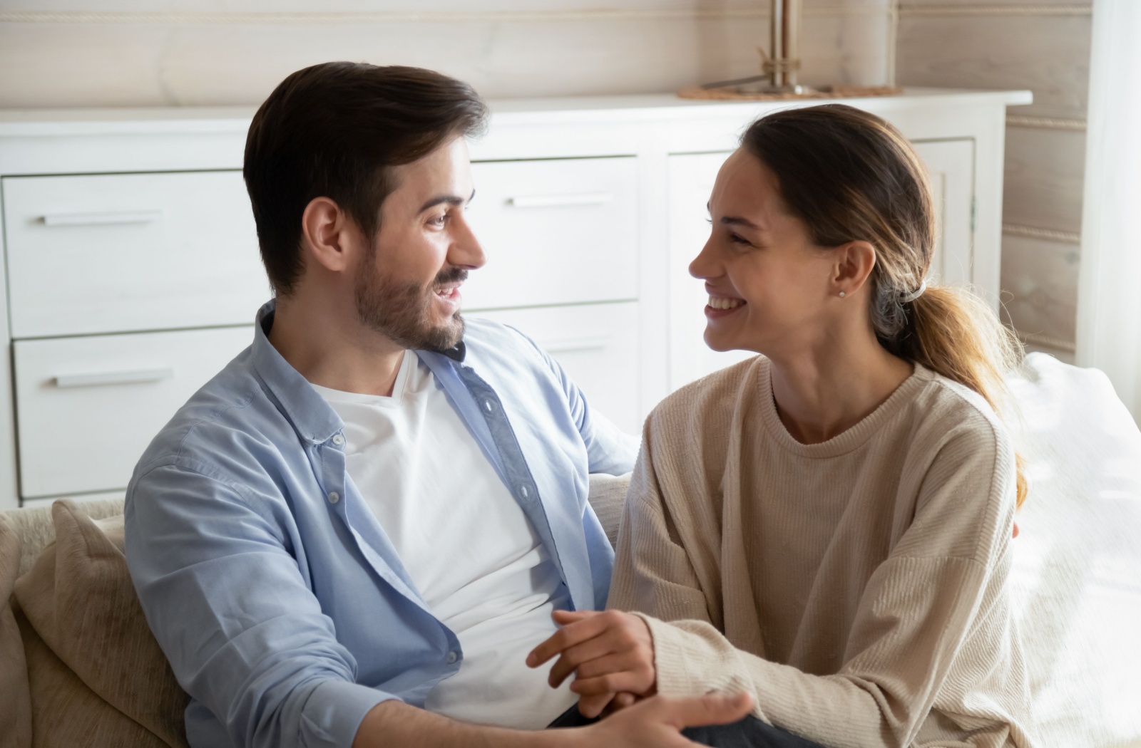 A man and a woman sitting on a couch, smiling and talking to each other.