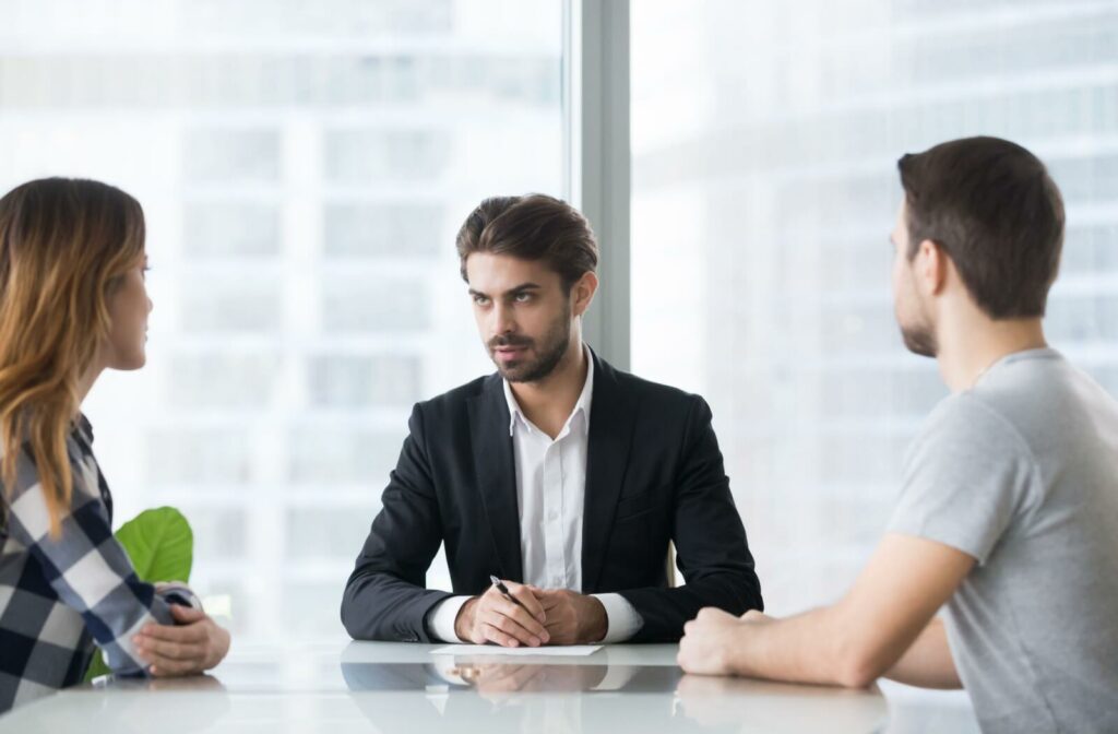 A couple sitting on opposite sides of a table with their mediator in between them discussing divorce terms