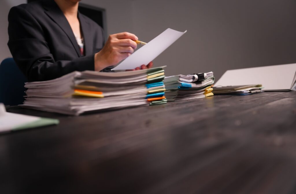 A stack of documents sits on a table. A lawyer is reviewing the documents during the due diligence process.